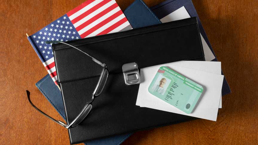 Green card, U.S. flag, and visa application paperwork for USCIS medical waiver